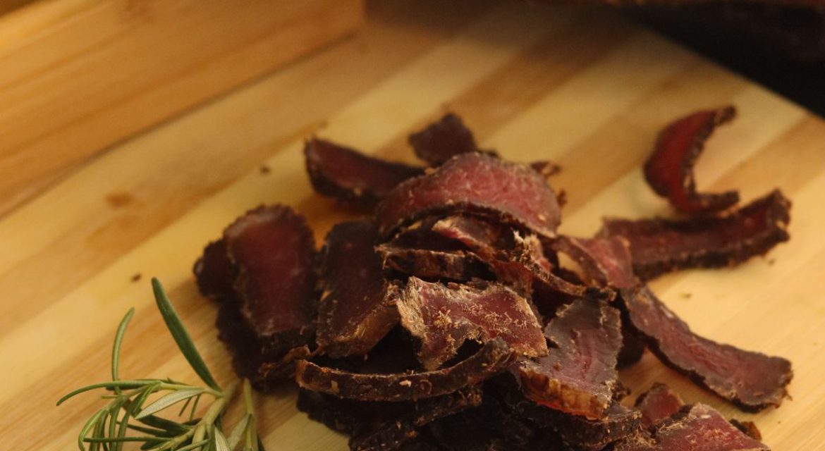 good biltong sliced on a wooden cutting board with a piece of uncut biltong on the side