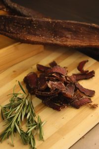 good biltong sliced on a wooden cutting board with a piece of uncut biltong on the side