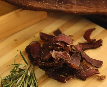 good biltong sliced on a wooden cutting board with a piece of uncut biltong on the side