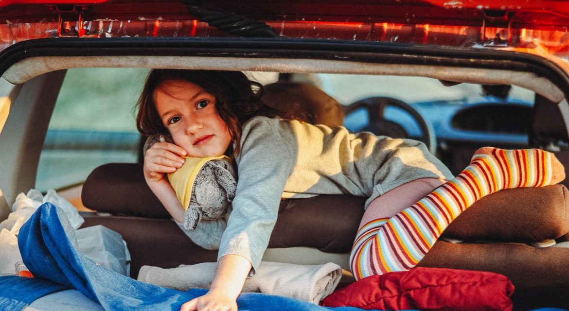 Child with colorful socks lying in a packed car trunk