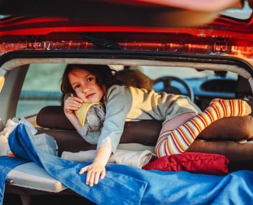Child with colorful socks lying in a packed car trunk