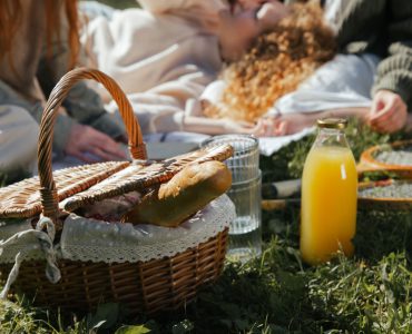 Picnic basket with bread, juice, and rackets on grass with people relaxing to illustrate a good picnic